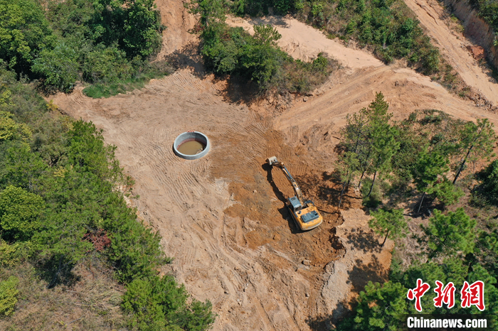 9月6日，在鄱陽湖畔的江西省九江市都昌縣多寶鄉(xiāng)林場，一臺挖掘機不停揮舞著“大臂”，為一口直徑5米、深8.5米的蓄水池進行場地平整，山泉水順著一根水管緩緩注入蓄水池內(nèi)。（無人機照片） <a target='_blank' href='/'>中新社</a>記者 劉占昆 攝