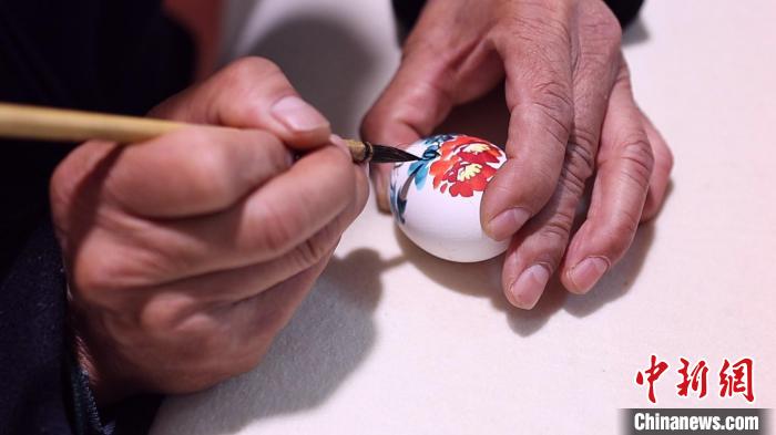 高觀凌一手拿蛋殼，一手持繪筆。片刻間，一朵美麗的牡丹花便“綻放”于蛋殼之上?！￡皷|明 攝